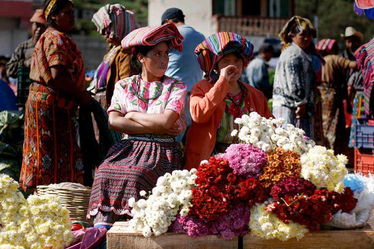 Women sell flowers in an outdoor market in Zunil, Guatemala, a small town near Quetzaltenango. At the market an announcer advertised items over a loudspeaker as farmers hurried around the square carrying huge bushels of vegetables.